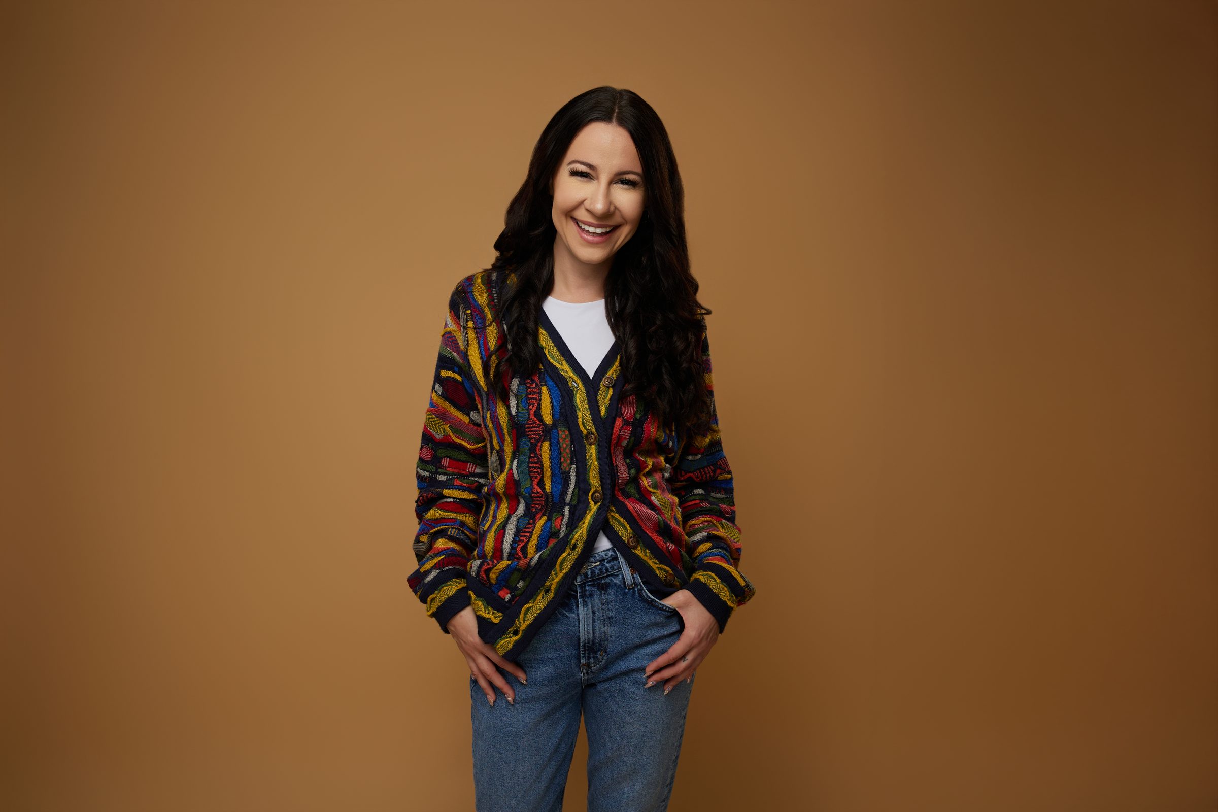 Bryanna Baptiste in a colorful striped Coogi cardigan, standing against a warm caramel backdrop